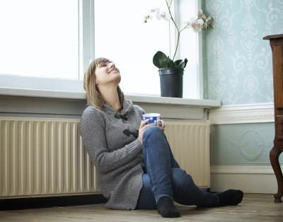 Une jeune femme est assise contre le radiateur dans sa maison pendant qu'elle se réchauffe avec une tasse de thé