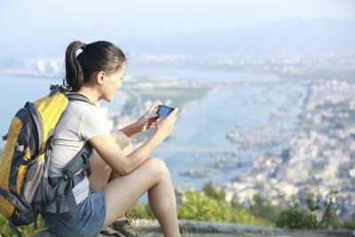 Une jeune femme utilise son téléphone intelligent tout en prenant une randonnée au-dessus de la ville.