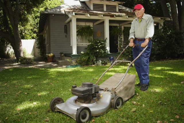 Un vieil homme est en train de tondre sa pelouse.
