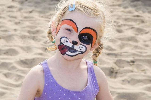 Une fille avec un visage peint en jouant dans le sable.