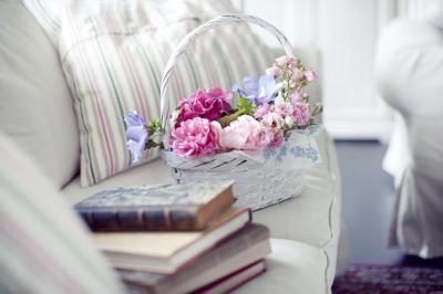 Un panier de fleurs sur un canapé blanc à côté d'une pile de livres anciens.