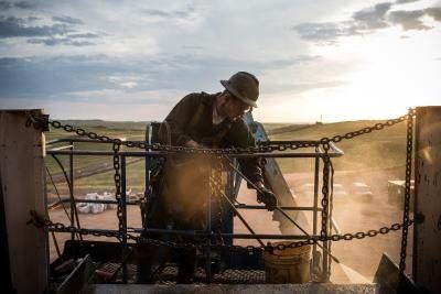 Un ouvrier travaille sur une plate-forme pétrolière avec le paysage du Dakota du Nord derrière lui.